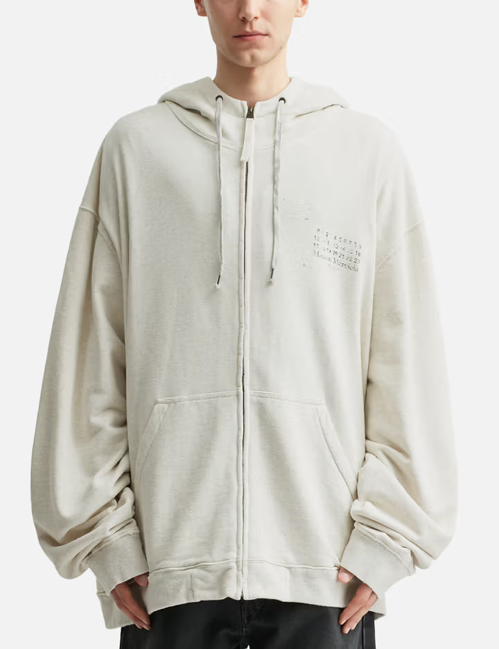 Sweat à capuche zippé pour homme, couleur écru, 100 % coton, avec logo estampé délavé et détails déstructurés.